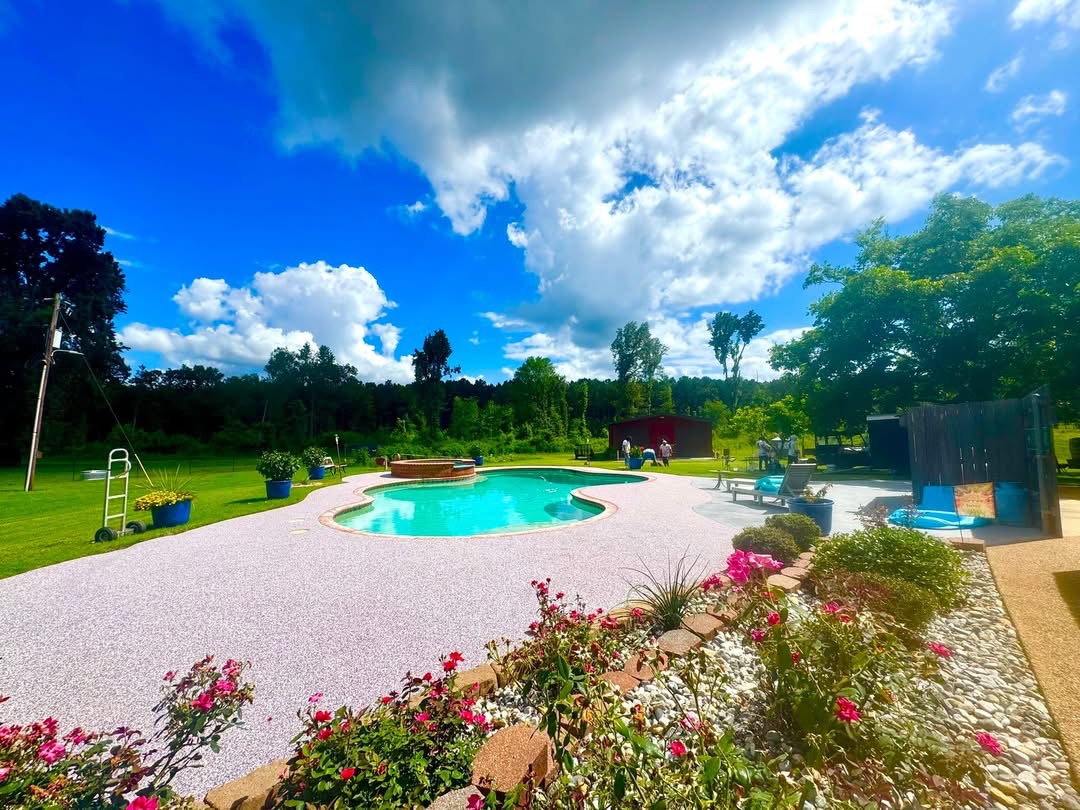 Bright daytime pool deck in pink speckled surfacing surrounded by flower beds