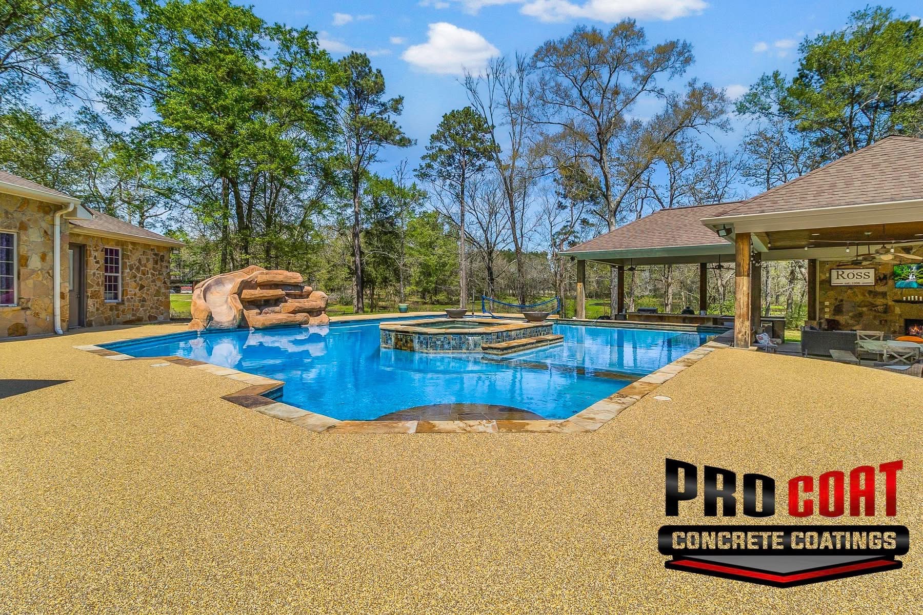 Tan speckled deck surfacing around a freeform pool with a rock waterslide and spa