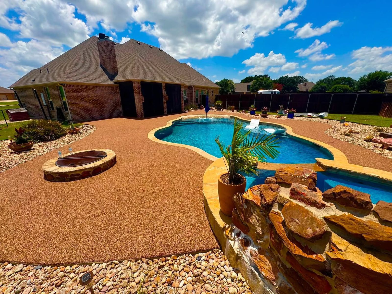 Same pool patio finished in tan and orange speckled surfacing with a stone waterfall feature