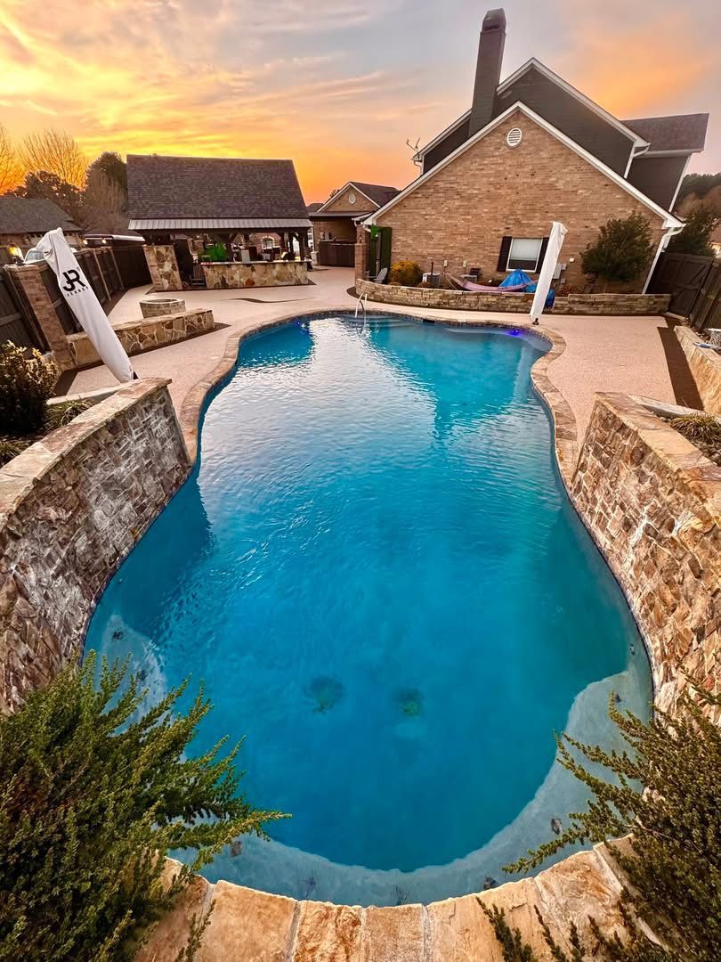 Finished pool deck in blue speckled surfacing with raised natural stone knee walls at sunset