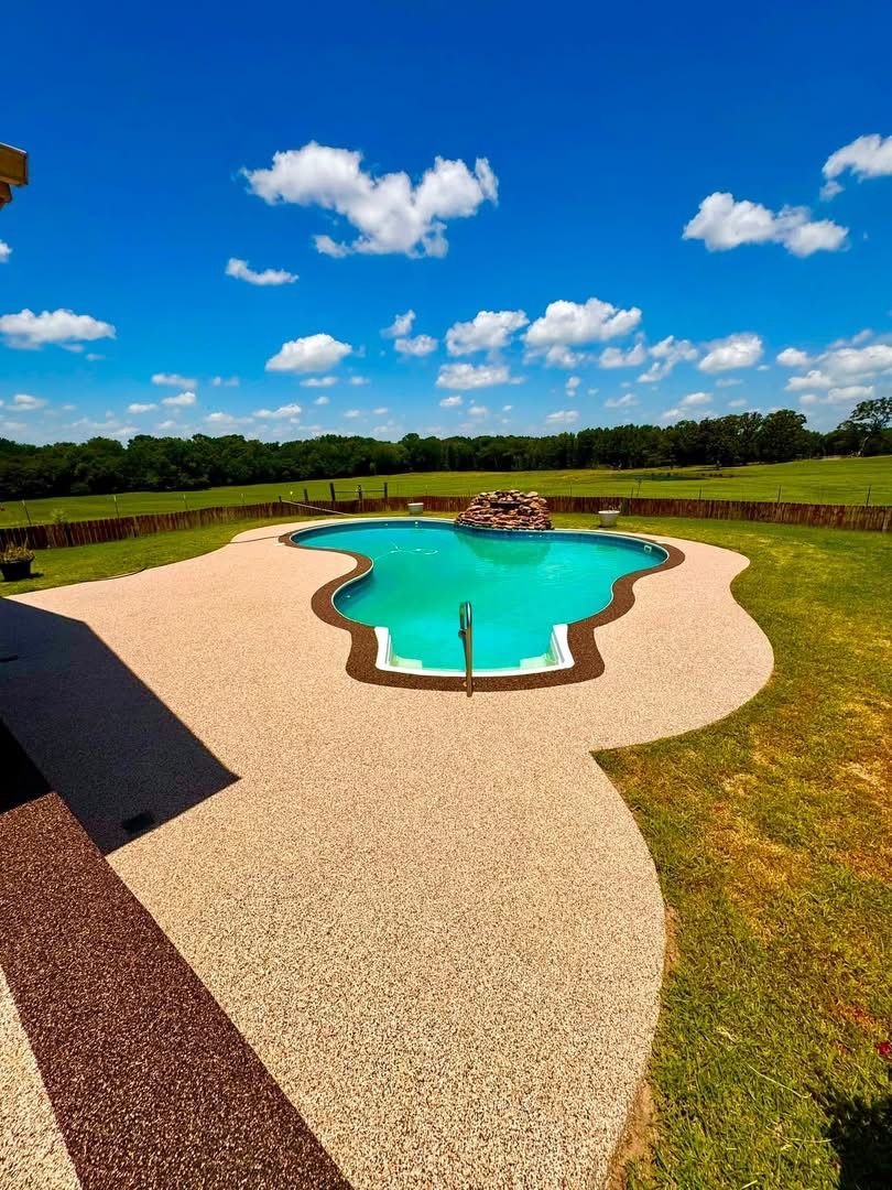 Aerial view of a tan speckled pool deck in an open grass field